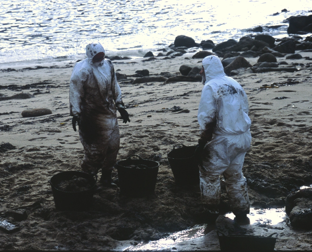 Zwei Menschen in Schutzanzügen reinigen einen Strand.